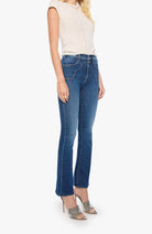 A model wearing a pair of medium-wash blue flare jeans, paired with a cream sleeveless top and gray high-heeled sandals, shown against a plain white background.