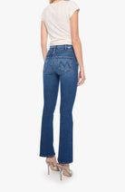 A woman shown from the back wearing blue flare jeans, a cream short-sleeve top, and metallic high heels against a plain light background.