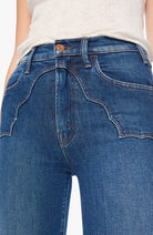 Close-up of a person wearing blue denim jeans with a white top, showing the back pocket and waistband details.
