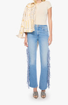 A model wearing light-wash blue flare jeans with long fringe detailing running down the outer sides, styled with a cream short-sleeve top and a patterned cream jacket, against a plain white background.