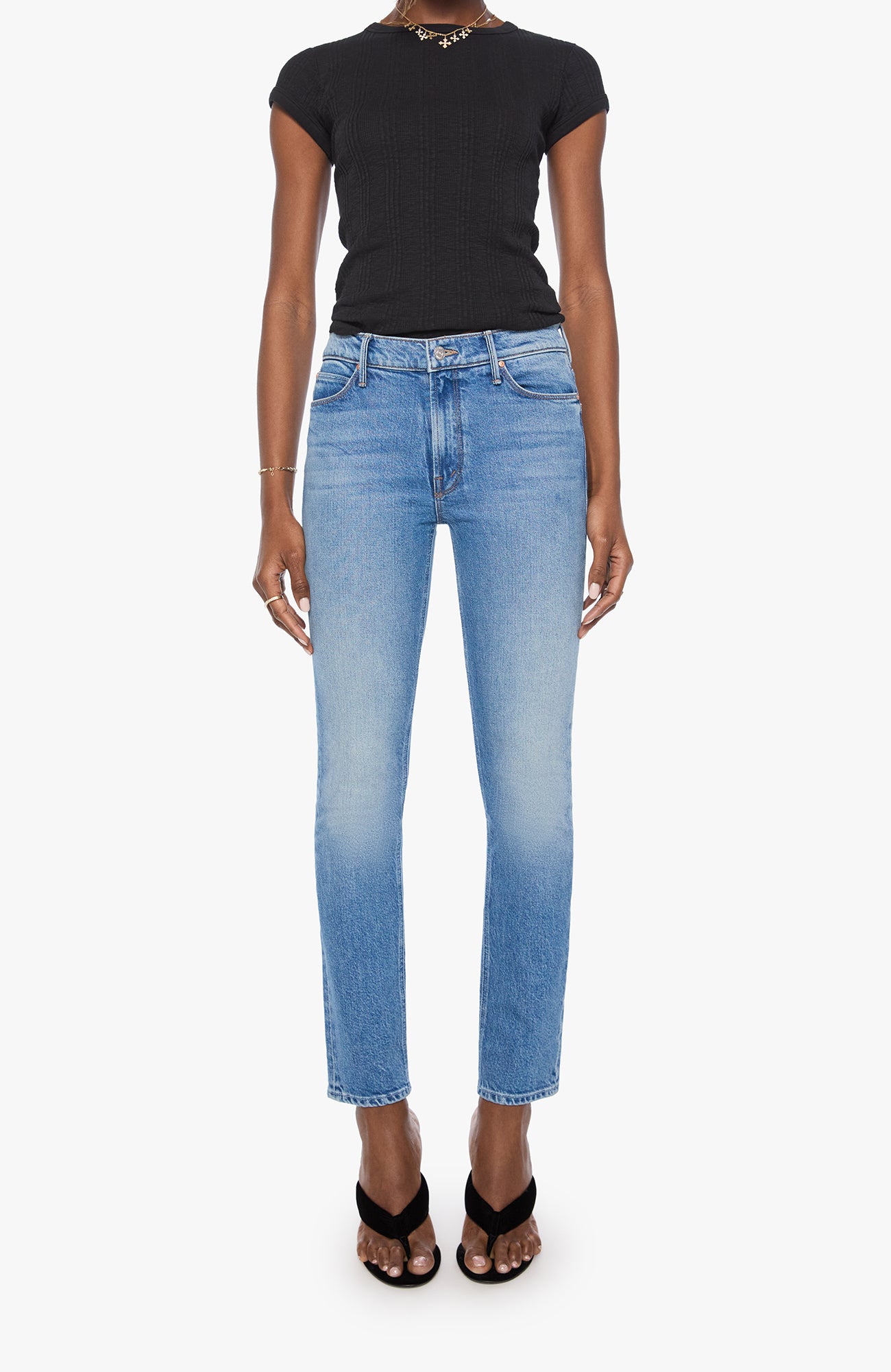 A model wearing light-wash blue cropped jeans, a black short-sleeve t-shirt, and black strappy heels, shown against a plain light gray studio background.