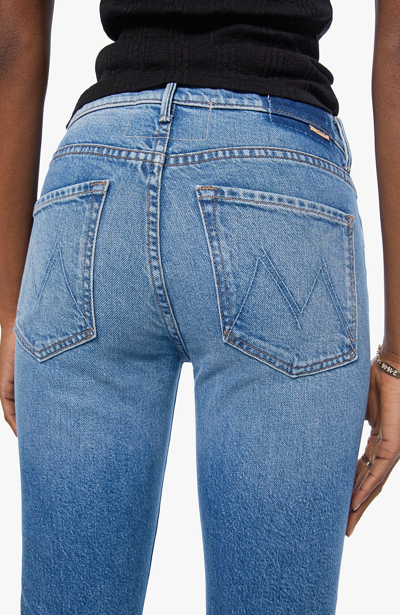 Close-up back view of a person wearing light blue denim jeans with a black top, showing the back pockets and waistband details.