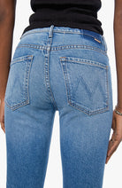Close-up back view of a person wearing light blue denim jeans with a black top, showing the back pockets and waistband details.
