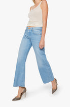 Woman wearing light blue jeans and a beige top on a white background