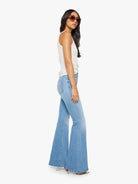 Woman wearing light blue flared jeans and a white top on a white background