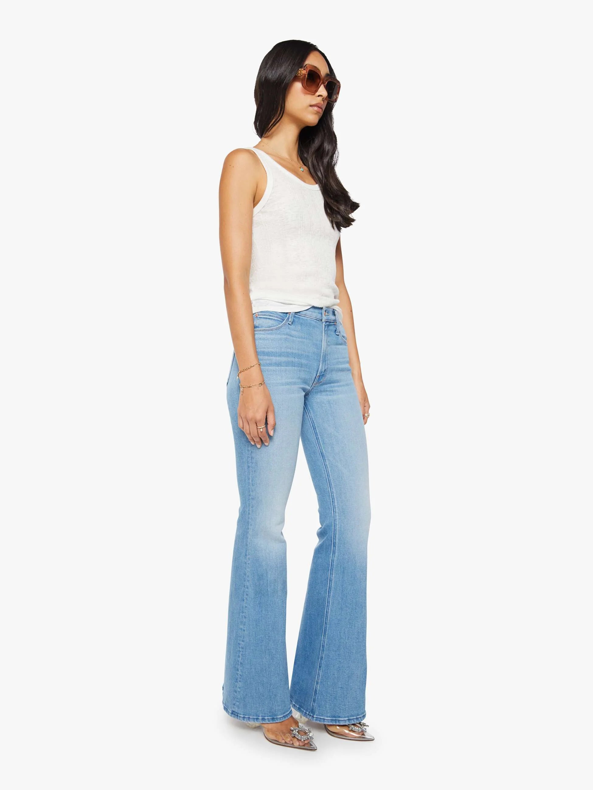 Woman wearing light blue flared jeans and a white top on a white background