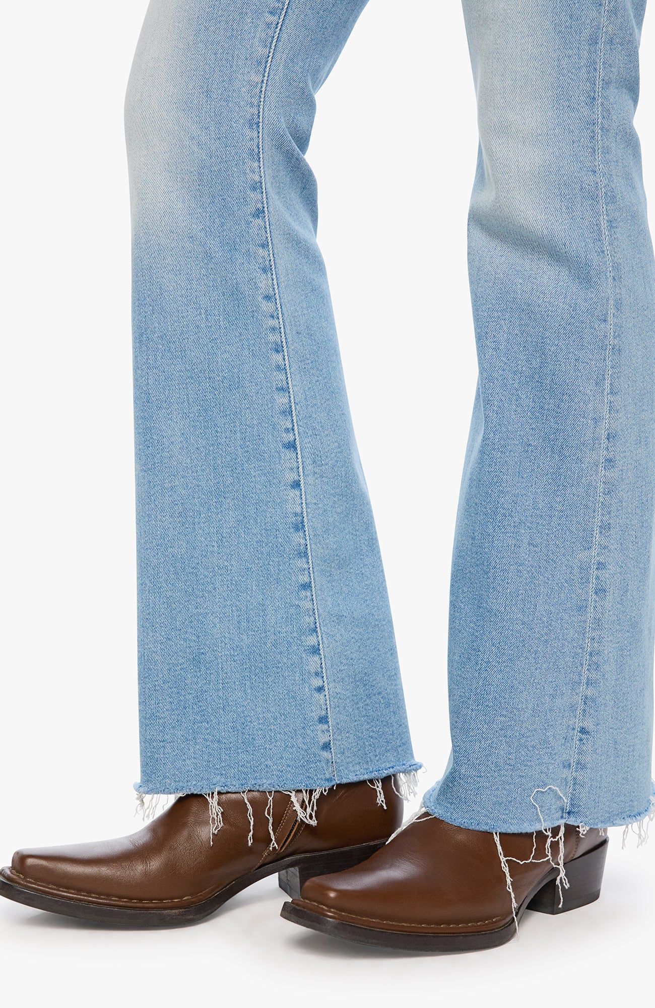 Close-up of a person's legs wearing light blue flared jeans with frayed hems and brown leather cowboy boots against a plain white background.
