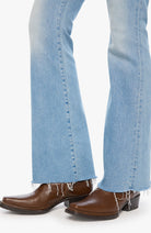 Close-up of a person's legs wearing light blue flared jeans with frayed hems and brown leather cowboy boots against a plain white background.