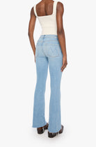 A model shown from the back wearing light-wash blue flare jeans, a cream tank top, and brown platform shoes against a plain white background.
