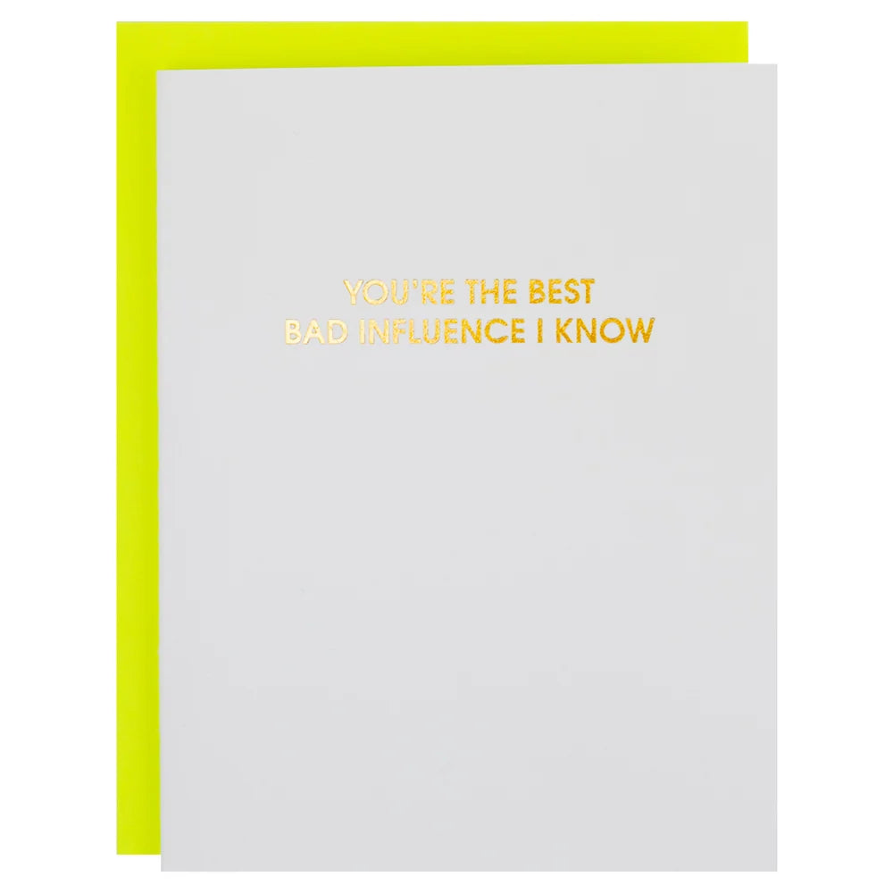 A white greeting card with gold foil text reading 'YOU'RE THE BEST BAD INFLUENCE I KNOW' and a bright yellow envelope behind it, shown on a white background.