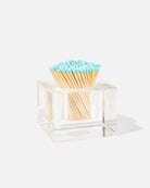 A clear acrylic square match holder filled with wooden matches that have light blue tips, photographed on a clean white background with a soft shadow.