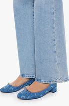 Person wearing blue denim shoes with white patterns and light blue jeans on a white background