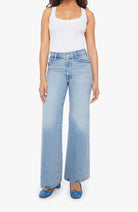 Woman wearing light blue flared jeans and a white tank top on a white background