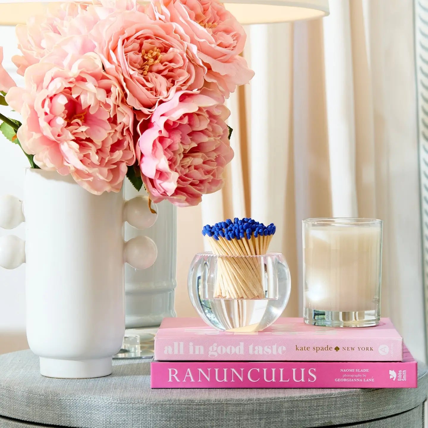 Pink flowers in a vase with books, matches, and a candle on a table.