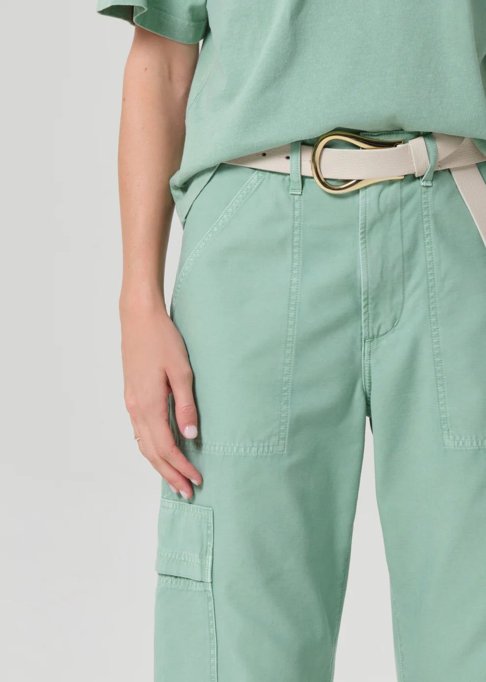 Person wearing a light green outfit with a belt on a plain background