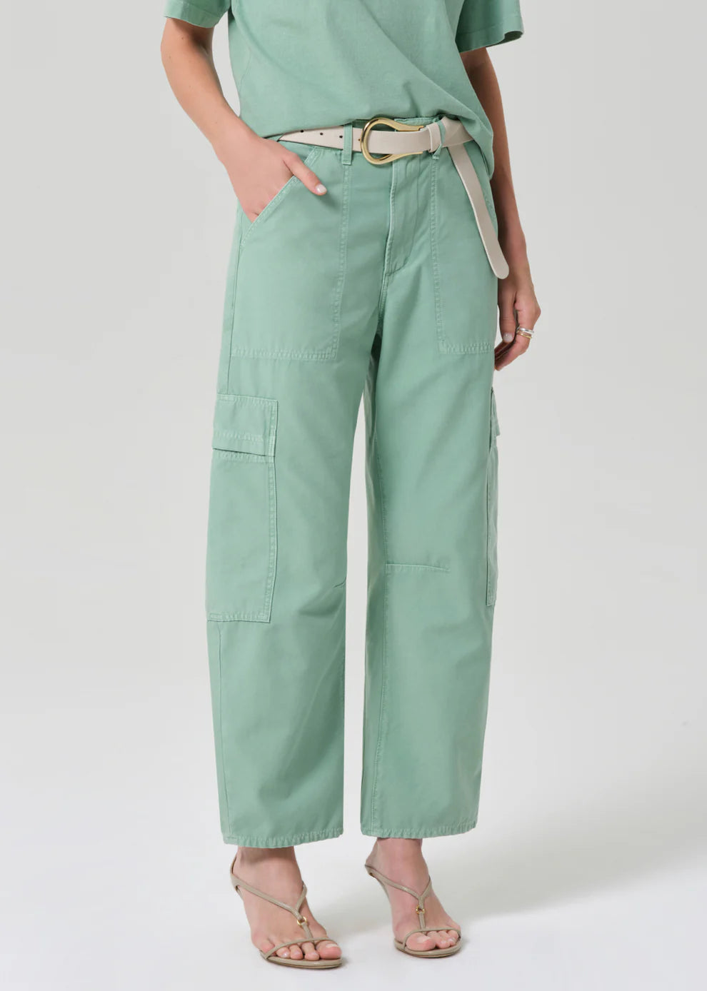 Person wearing light green cargo pants with a belt on a white background
