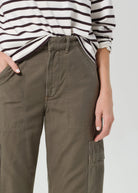 Person wearing olive green cargo pants with a striped shirt on a white background