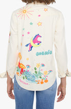 A woman shown from the back wearing a cream-colored long-sleeve button-up shirt with colorful embroidered designs, including a unicorn, stars, flowers, and the words 'cosmic' and 'MOTHER'. She is wearing blue jeans against a plain white background.