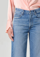 Person wearing light blue jeans and a pink shirt against a gray background