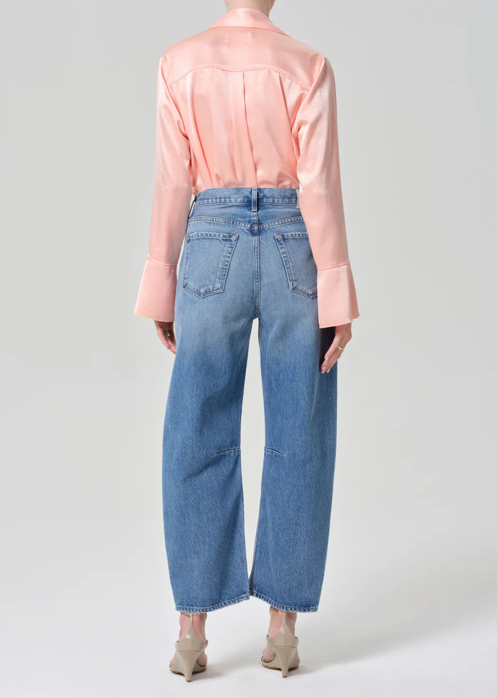 Person wearing a light pink blouse and blue jeans on a plain background