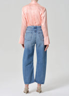 Person wearing a light pink blouse and blue jeans on a plain background