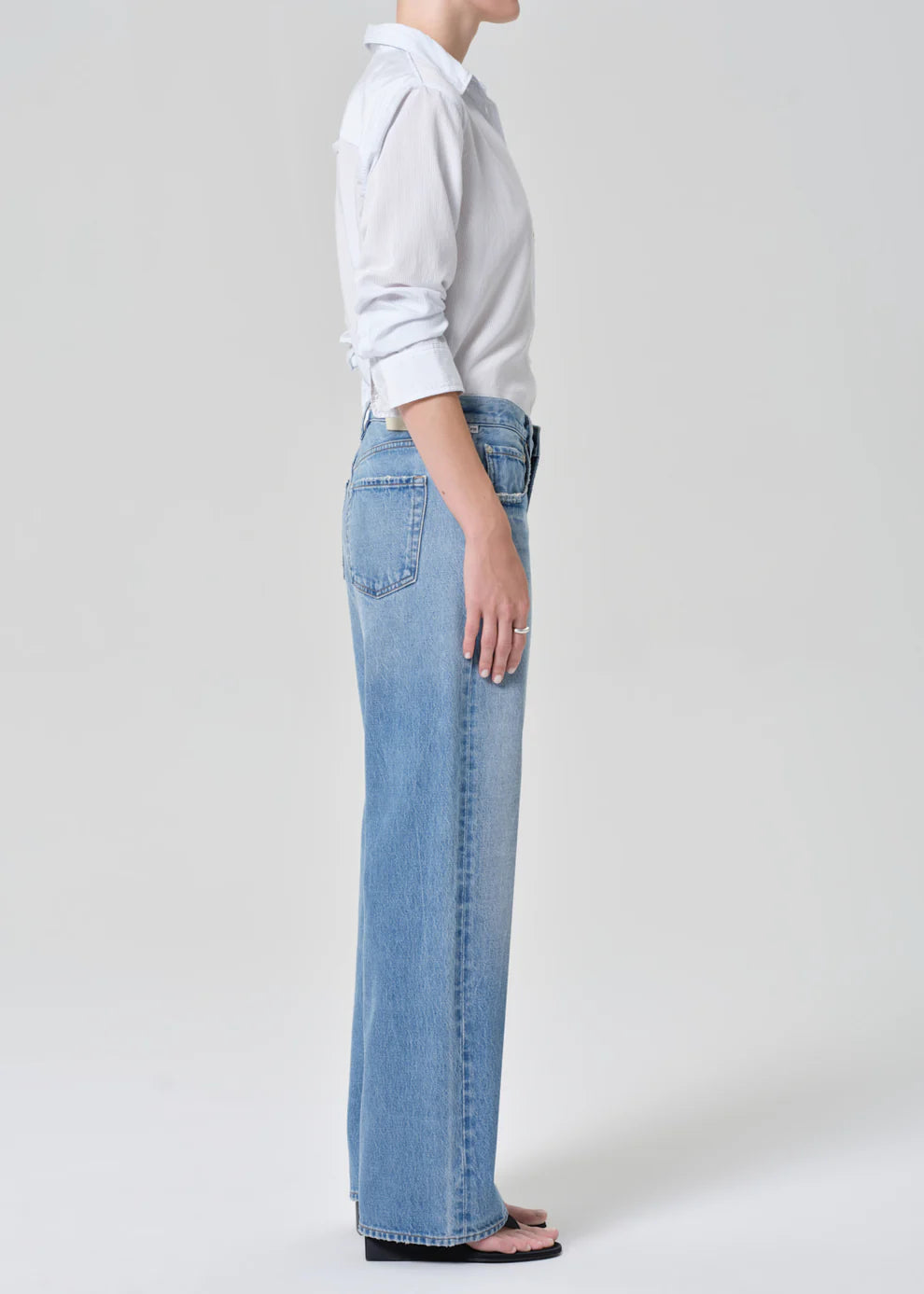 Person wearing light blue jeans and a white shirt on a plain background
