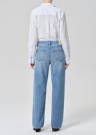 Person wearing a white shirt and light blue jeans on a plain background