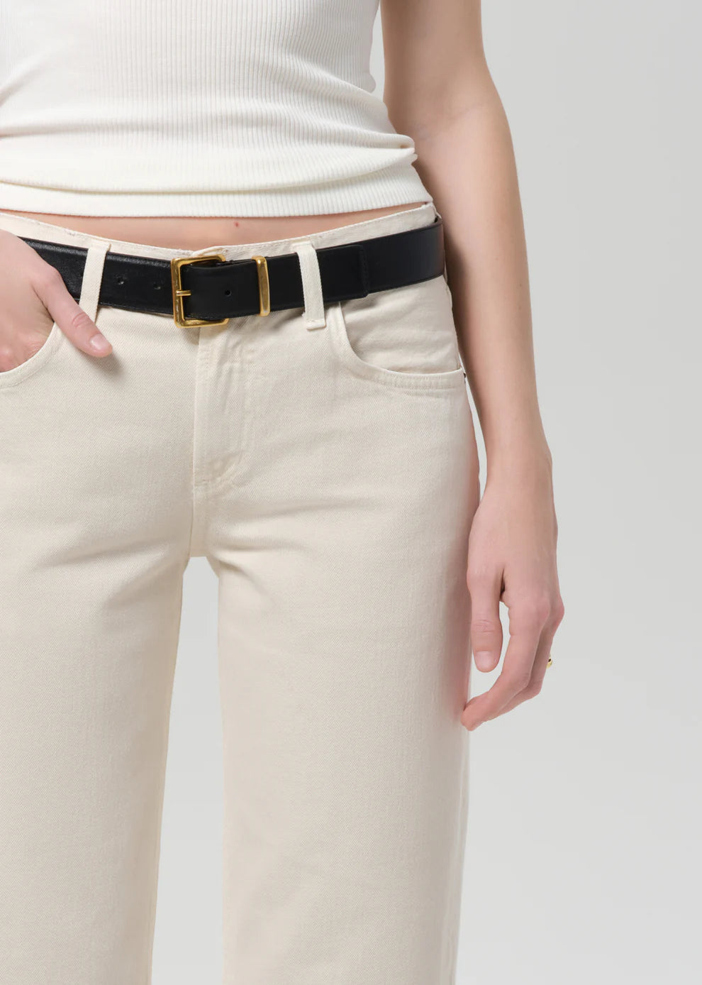 Person wearing a black belt with a gold buckle on beige pants against a white background