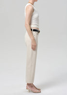 Person wearing a white sleeveless top and beige pants on a plain background
