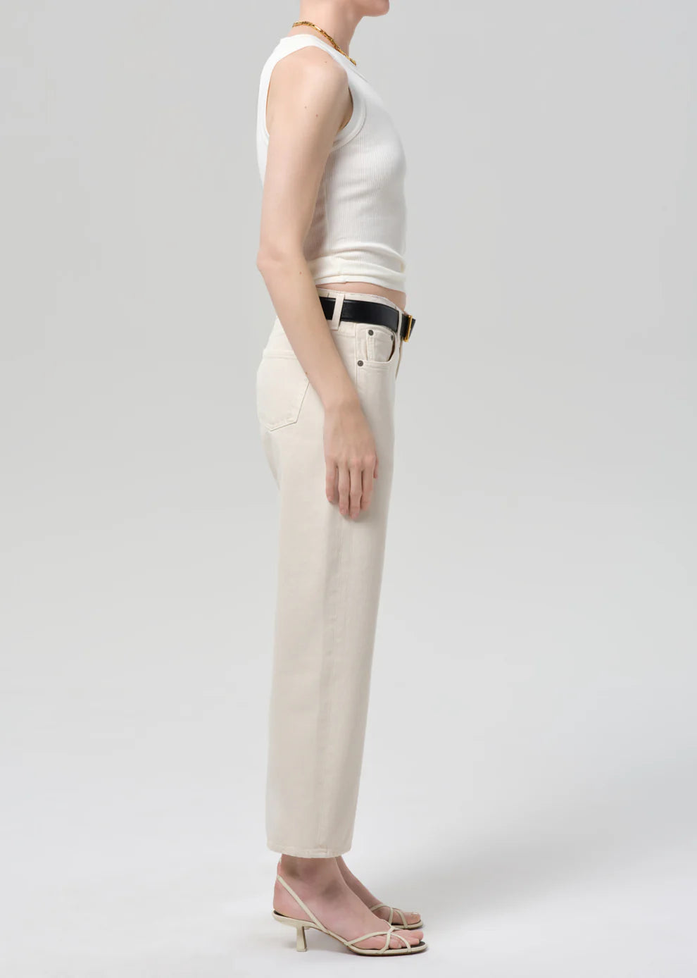 Person wearing a white sleeveless top and beige pants on a plain background