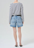 Person wearing a striped sweater and denim shorts on a white background