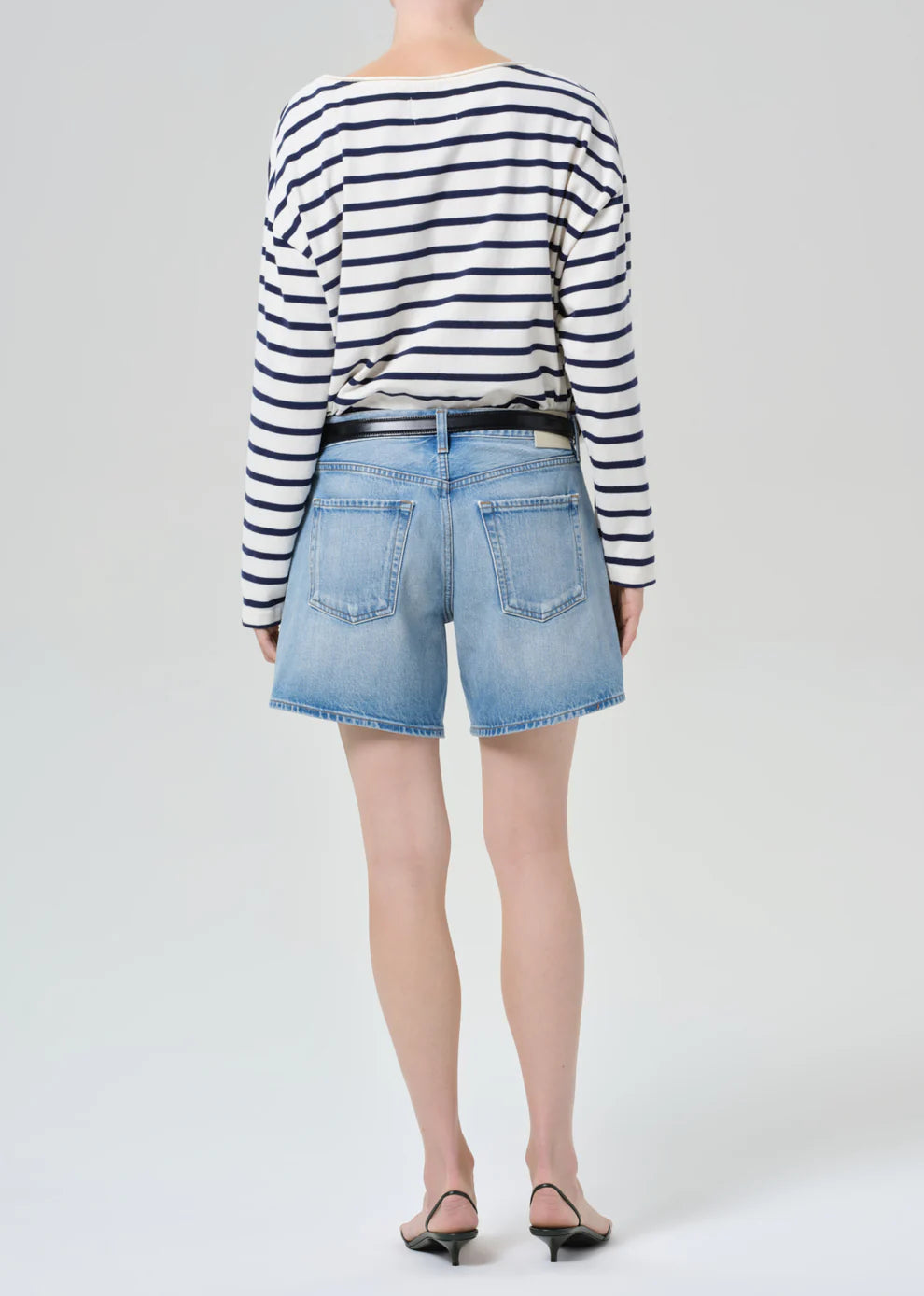 Person wearing a striped sweater and denim shorts on a white background