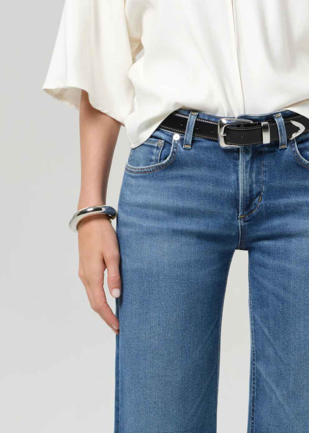 Person wearing blue jeans and a white shirt with a plain background