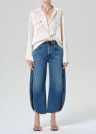 Person wearing a white blouse and blue jeans on a plain background