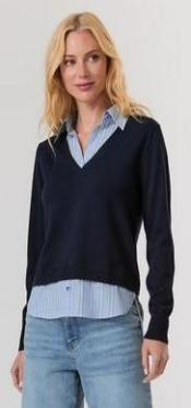 Woman wearing a navy sweater over a light blue shirt with light blue jeans on a white background