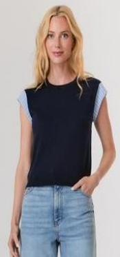 Woman wearing a black sleeveless top with light blue accents and light blue jeans on a white background