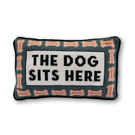 Decorative pillow with 'The Dog Sits Here' text and bone patterns on a white background