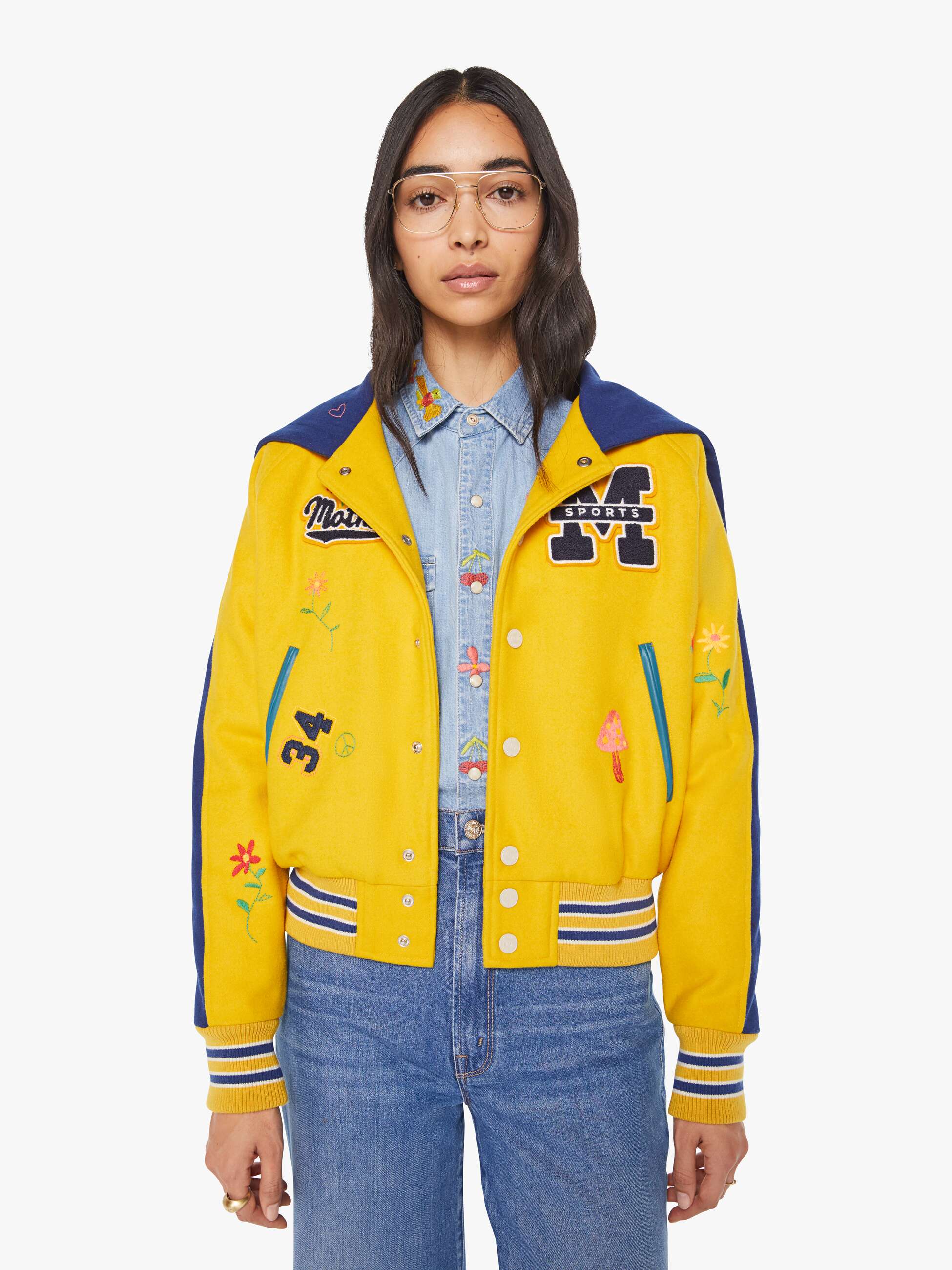 Person wearing a yellow varsity jacket with blue accents and colorful patches on a white background