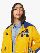 Person wearing a yellow varsity jacket with patches on a white background