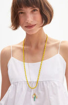 Woman wearing a white dress with a long yellow necklace against a white background
