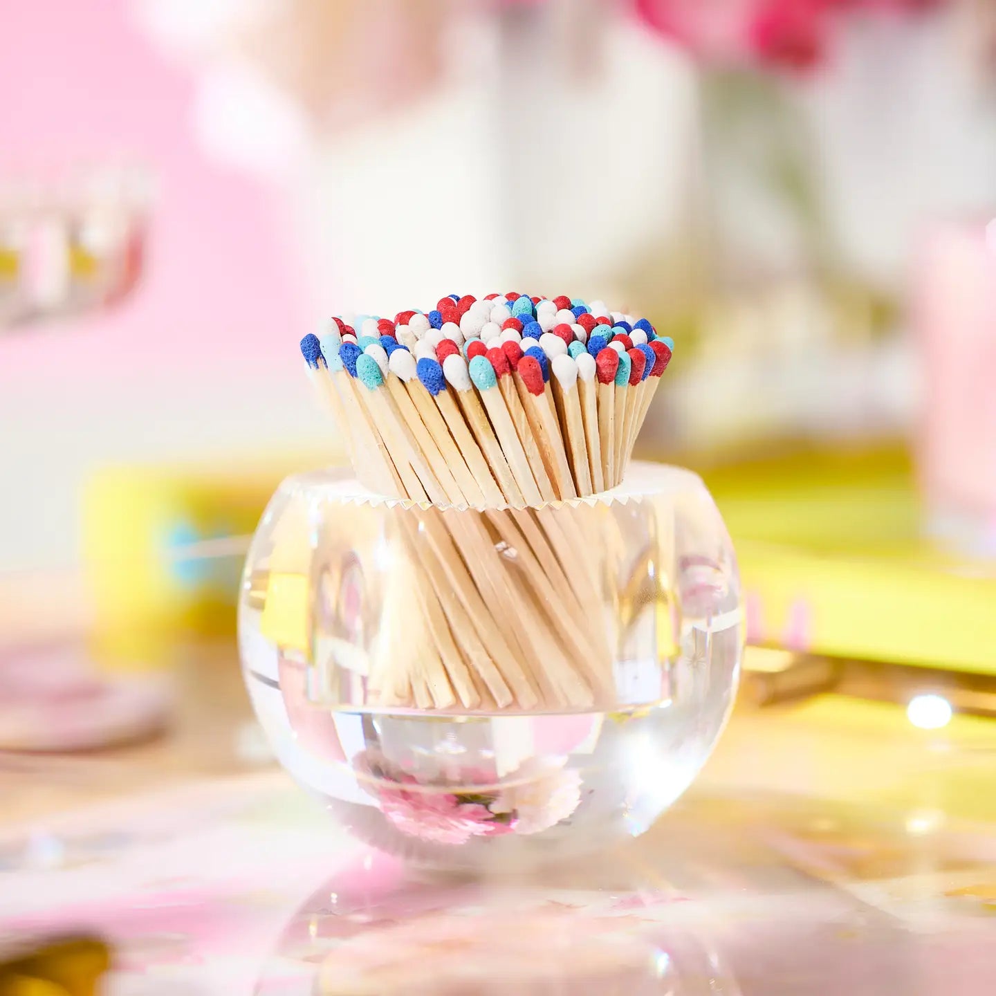 Colorful matchsticks in a clear glass holder on a blurred background