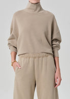 Person wearing a beige turtleneck sweater and pants on a light gray background