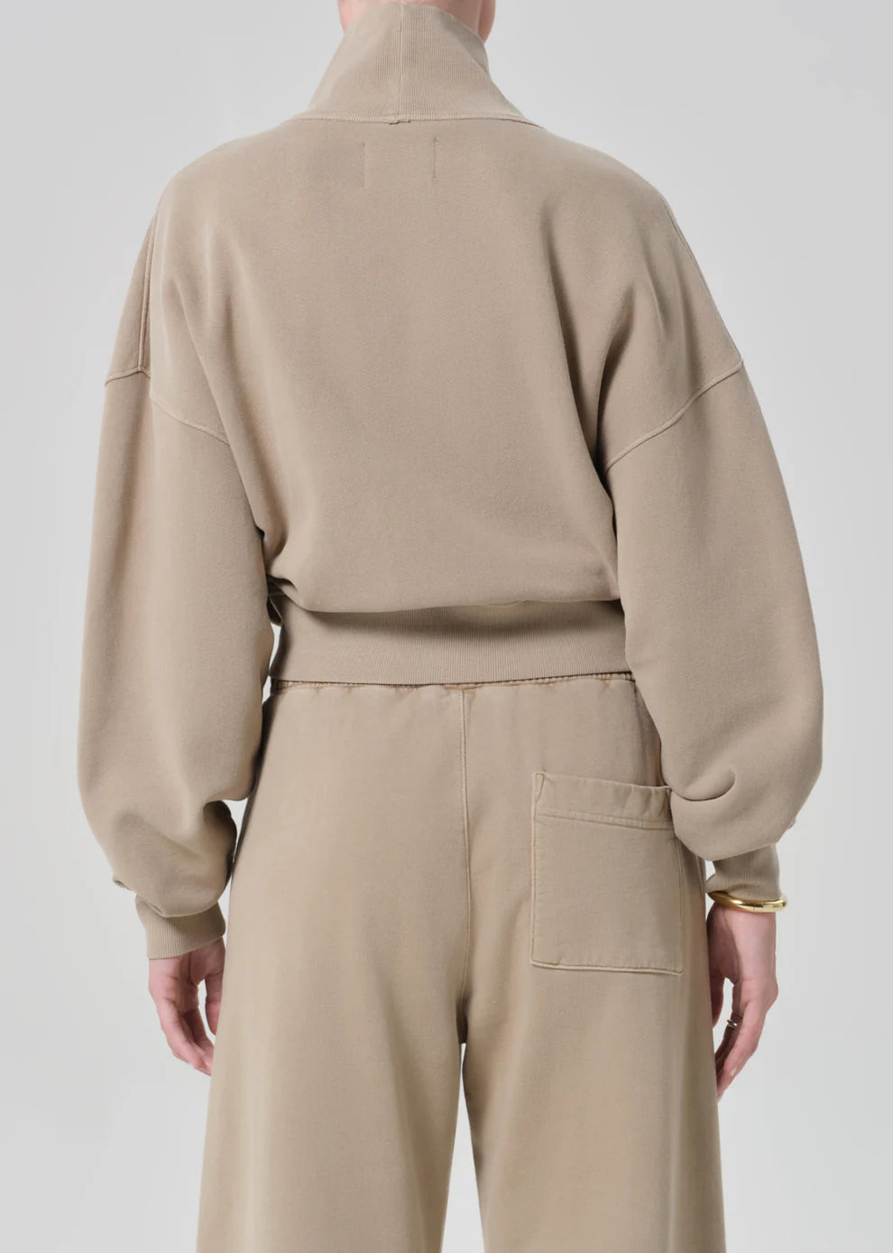 Person wearing a beige tracksuit on a plain background