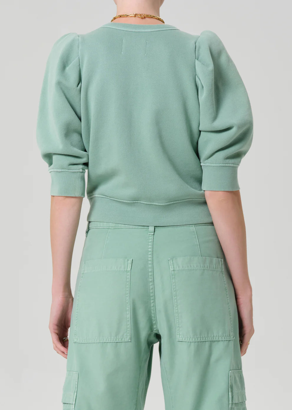 Person wearing a mint green outfit with a matching sweater and pants on a light gray background