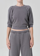 Person wearing a gray cropped sweatshirt and pants on a light gray background