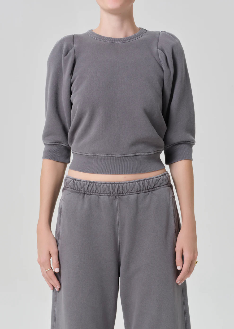 Person wearing a gray cropped sweatshirt and pants on a light gray background