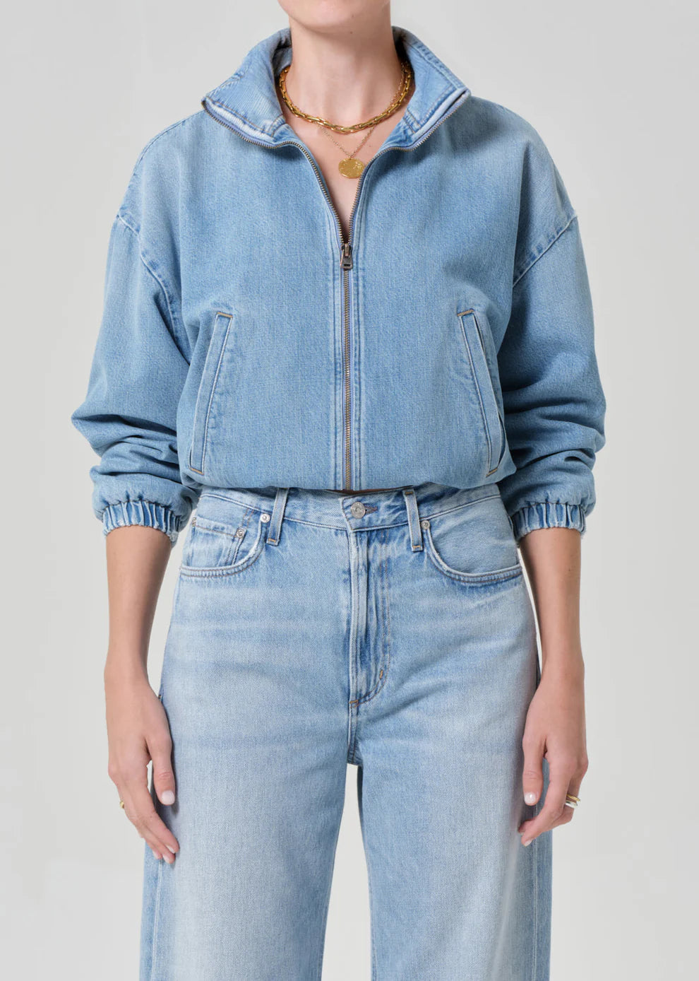 Person wearing a light blue denim jacket and jeans on a plain background