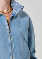 Close-up of a person wearing a blue denim jacket with a plain background
