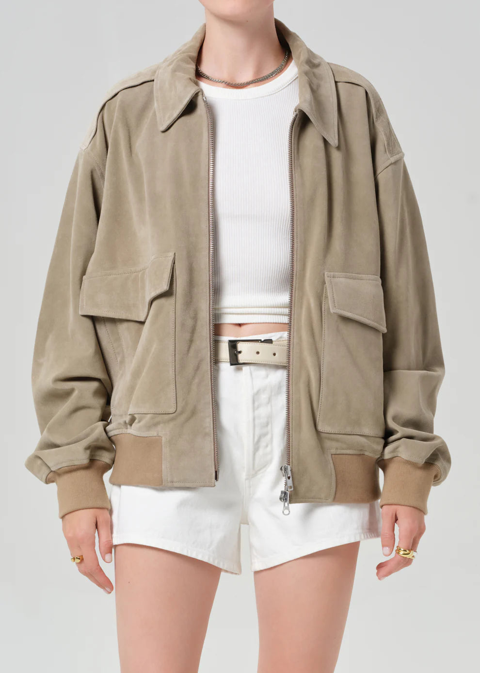 Person wearing a beige jacket over a white shirt and shorts on a light gray background