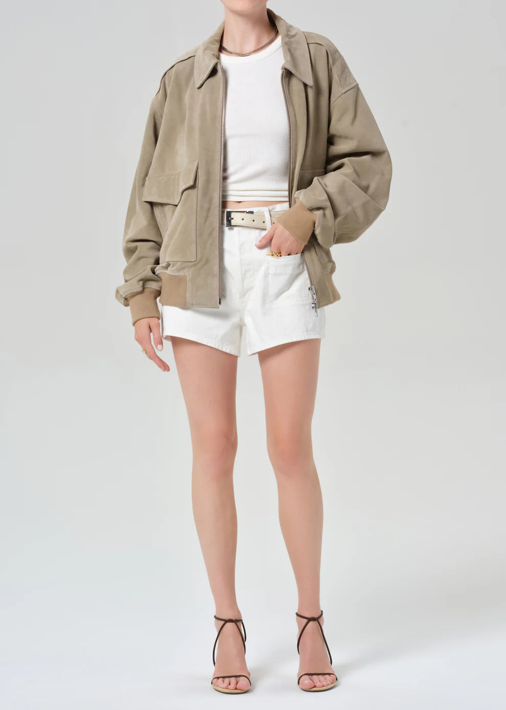 Person wearing a beige jacket, white shirt, and shorts on a plain background